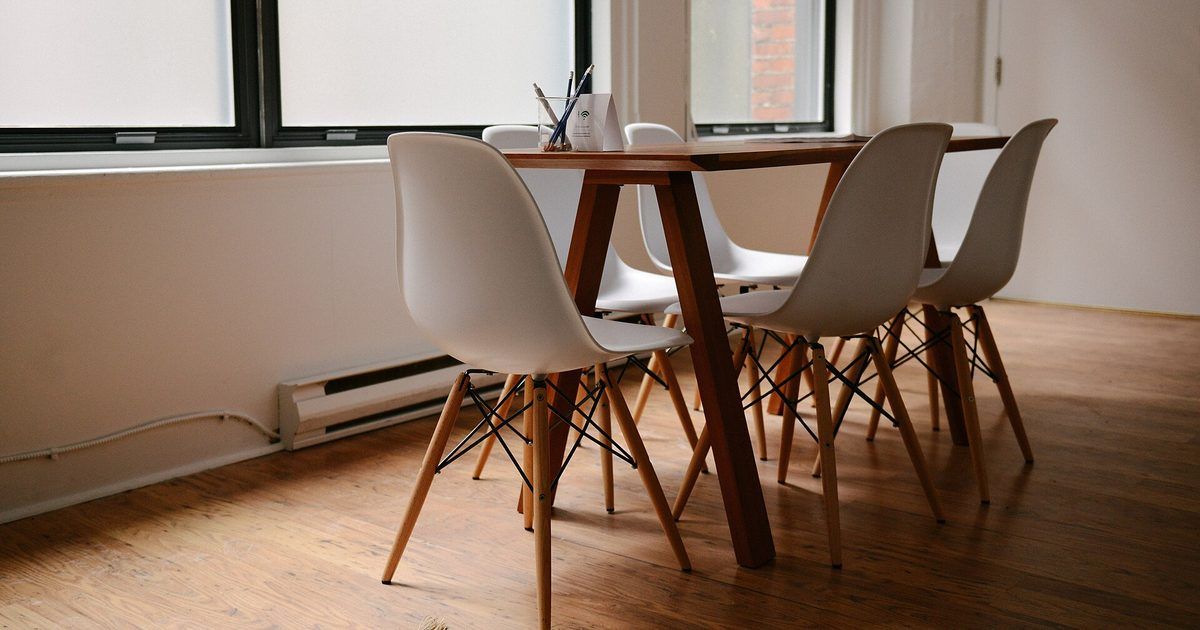 Mesa de madera con sillas blancas junto a una ventana, sobre piso de madera