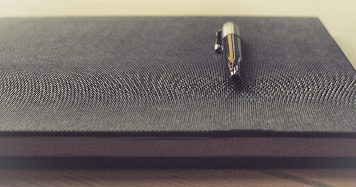Bolígrafo metálico sobre un cuaderno de tapa gris, sobre una mesa de madera